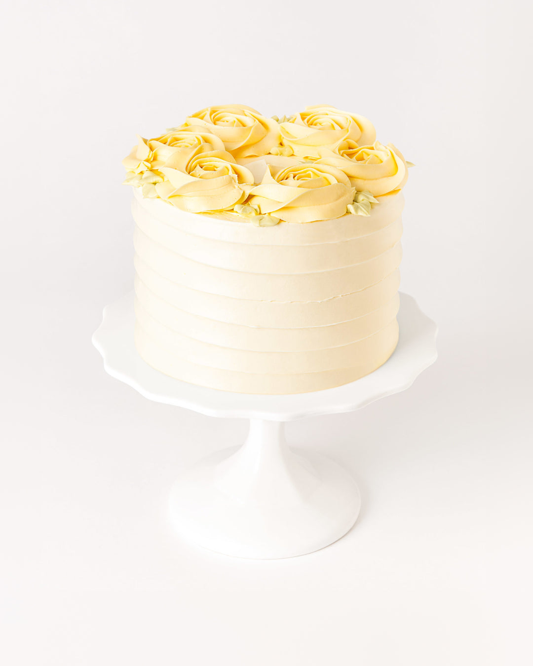 Mango passionfruit layer cake with buttercream roses on a white cake stand