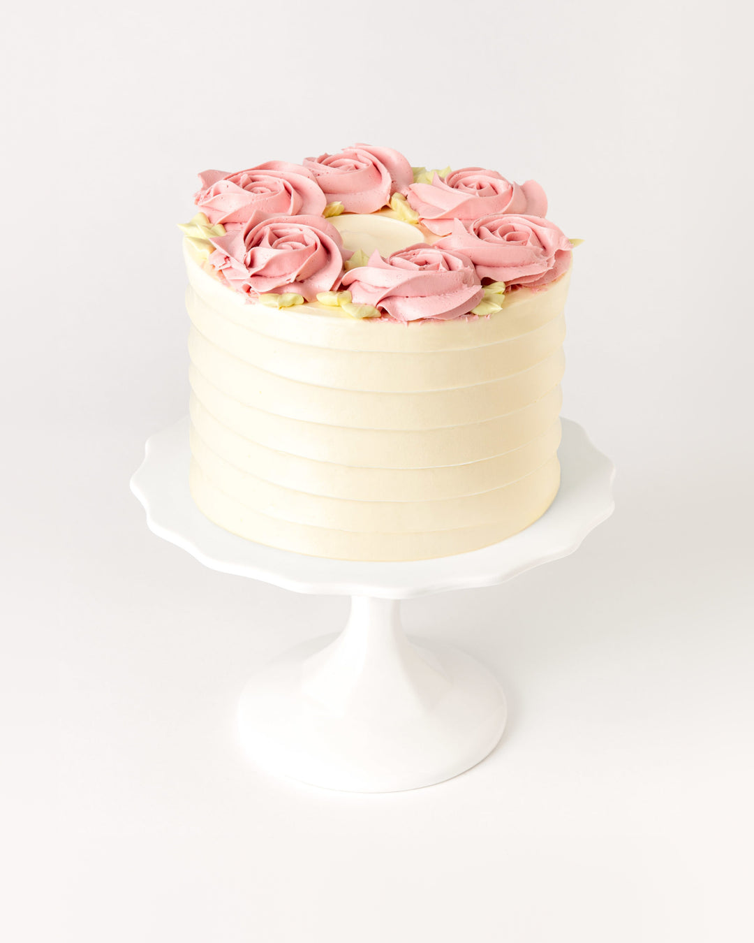 Raspberry vanilla cake with pink buttercream rosettes on a white cake stand