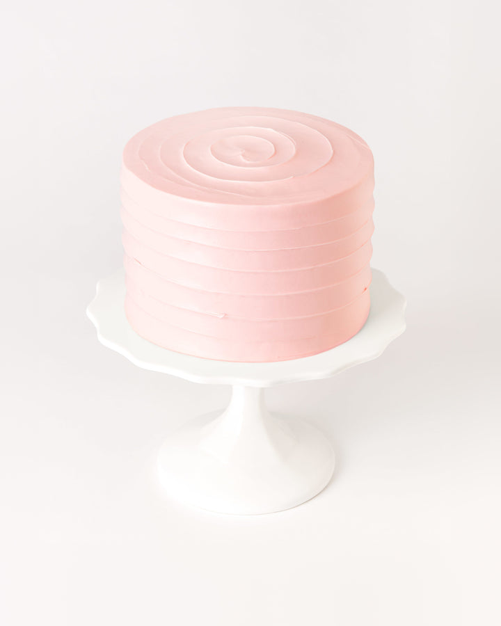 Pastel pink tinted buttercream swirl cake on a white cake stand