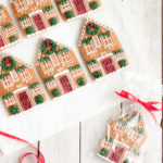 Victorian gingerbread house cookies featuring detailed royal icing designs, red doors, wreaths, and greenery, individually wrapped with ribbons.