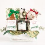 A holiday-themed gift basket filled with festive treats, including chocolate cookies, caramel corn, English toffee, peppermint bark, hot chocolate mix, vanilla marshmallows, holiday meringues, a gingerbread cookie, and salted caramels in a bauble.