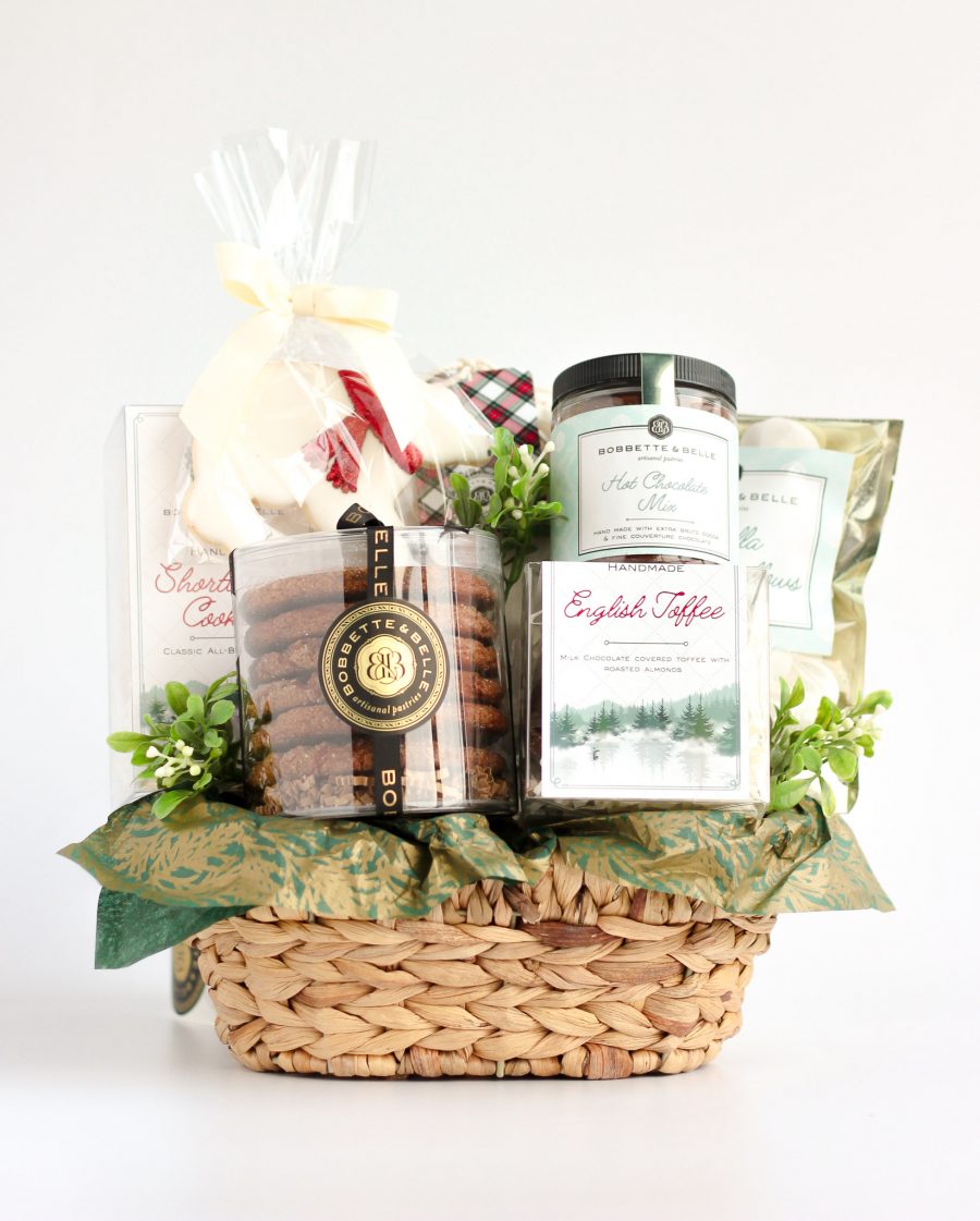 A woven holiday gift basket filled with gourmet treats, including ginger cookies, caramel corn, English toffee, shortbread, hot chocolate, marshmallows, and a decorative polar bear sugar cookie.