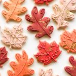 Thanksgiving-themed sugar cookies shaped like oak and maple leaves in fall colours, with a squirrel and glittering acorn, packaged in clear bags with ribbon ties