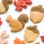 Thanksgiving-themed sugar cookies shaped like oak and maple leaves in fall colours, with a squirrel and glittering acorn, packaged in clear bags with ribbon ties