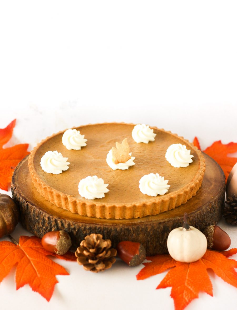 Homemade Thanksgiving pumpkin pie with a buttery crust, smooth spiced pumpkin filling, topped with whipped cream and shortbread cookie leaves