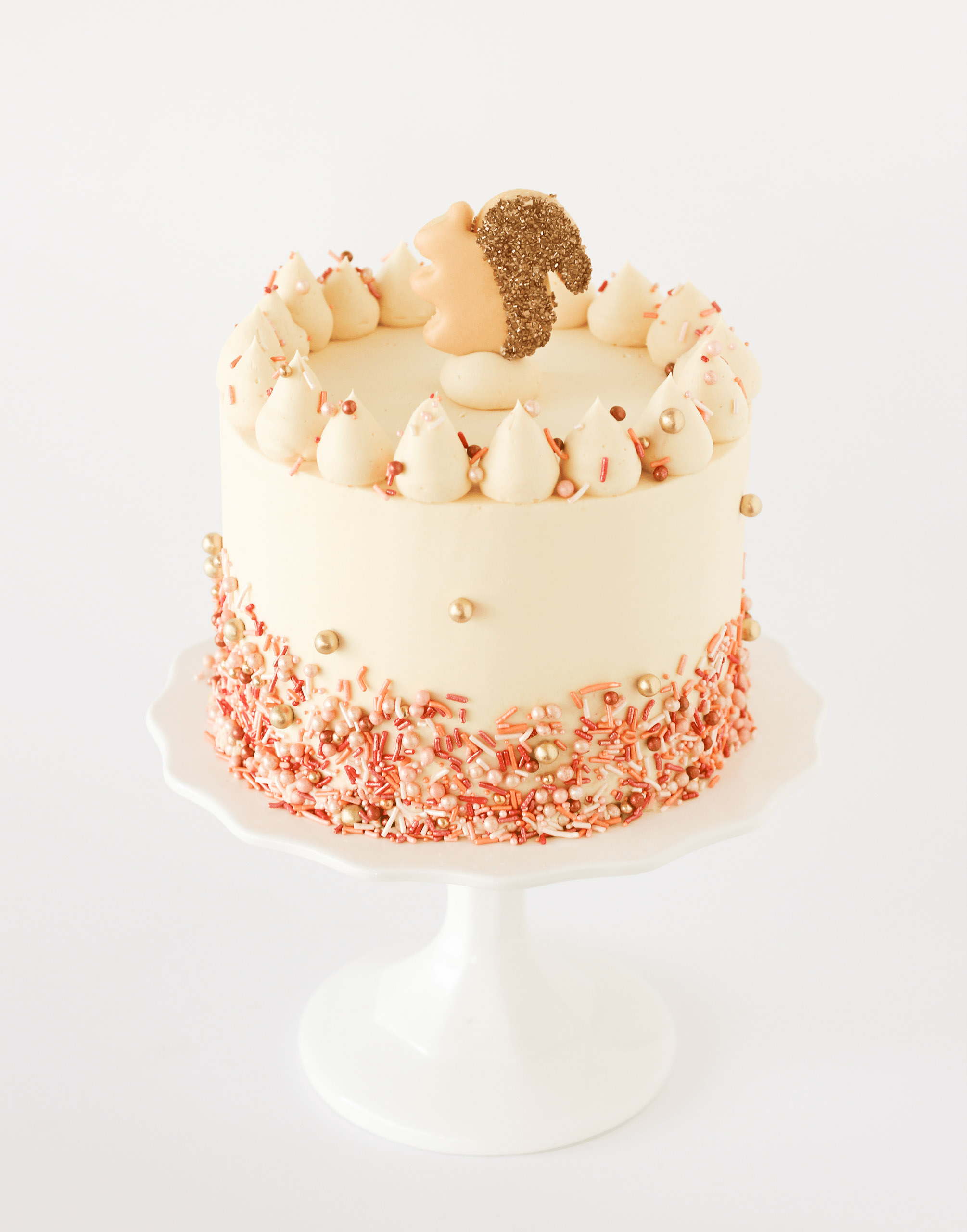 Three-layer pumpkin spice cake with maple caramel buttercream, topped with fall sprinkles and a sugar cookie squirrel, perfect for Thanksgiving celebrations