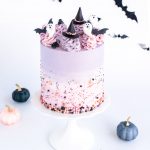 Halloween cake decorated with pastel purple ombre frosting, fondant ghosts, witch hats, and bats, with festive sprinkles