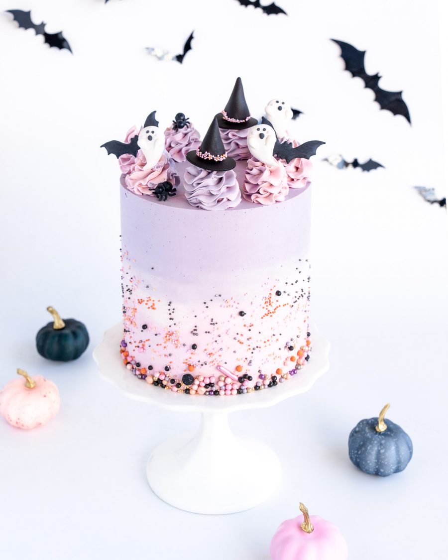 Halloween cake decorated with pastel purple ombre frosting, fondant ghosts, witch hats, and bats, with festive sprinkles