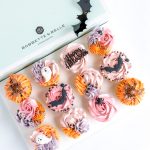 An open package of 12 decorative Halloween themed cupcakes in shades of orange, pink, purple and black.