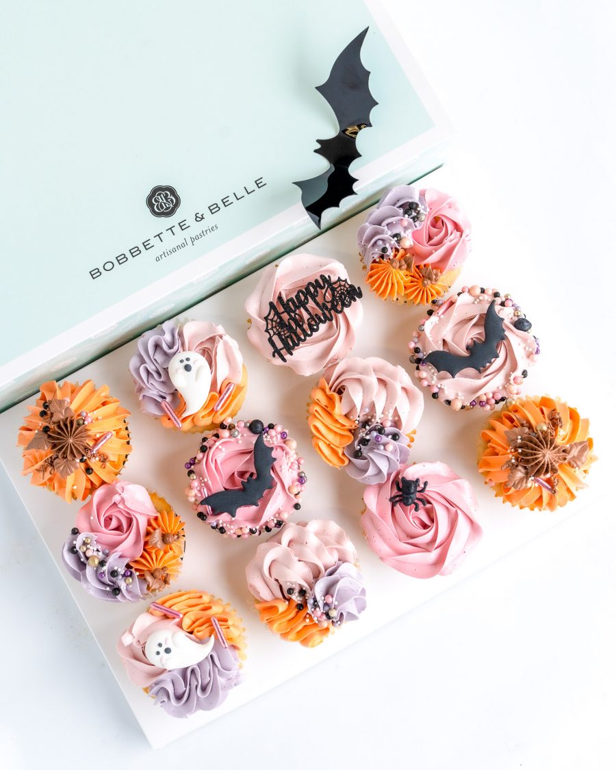 An open package of 12 decorative Halloween themed cupcakes in shades of orange, pink, purple and black.