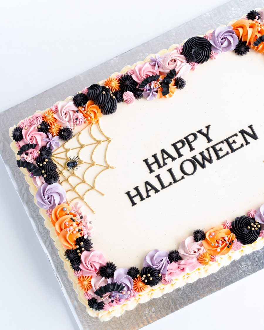 A rectangular sheet cake decorated for Halloween, with a smooth white icing base and a colorful buttercream border. The border features intricate piping in shades of orange, black, purple, and pink, forming a festive and playful design. On one corner, a gold spider web is piped delicately, complete with a small decorative spider. The center of the cake displays the words "Happy Halloween" in a bold, elegant font, creating a clean and stylish look. The cake sits on a silver cake board, making it a beautiful centerpiece for any Halloween gathering.