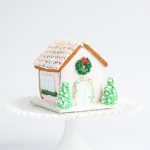 A fully assembled gingerbread house decorated with royal icing, sugar dragees, a piped wreath, and sparkling sugar snow, sitting on a festive board.