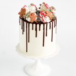 Festive holiday drip cake topped with gingerbread cookies, candy canes, whipped frosting swirls, and chocolate ganache drips.