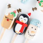 Holiday-themed cake popsicles featuring hand-decorated designs of a reindeer with holly accents, a penguin with a red scarf and Santa hat, and a snowman with a blue knitted hat and snowflake decoration.