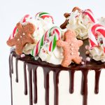 Close-up view of a festive Christmas cake decorated with chocolate ganache drips, tiny gingerbread men, and candy canes, showcasing intricate holiday details.