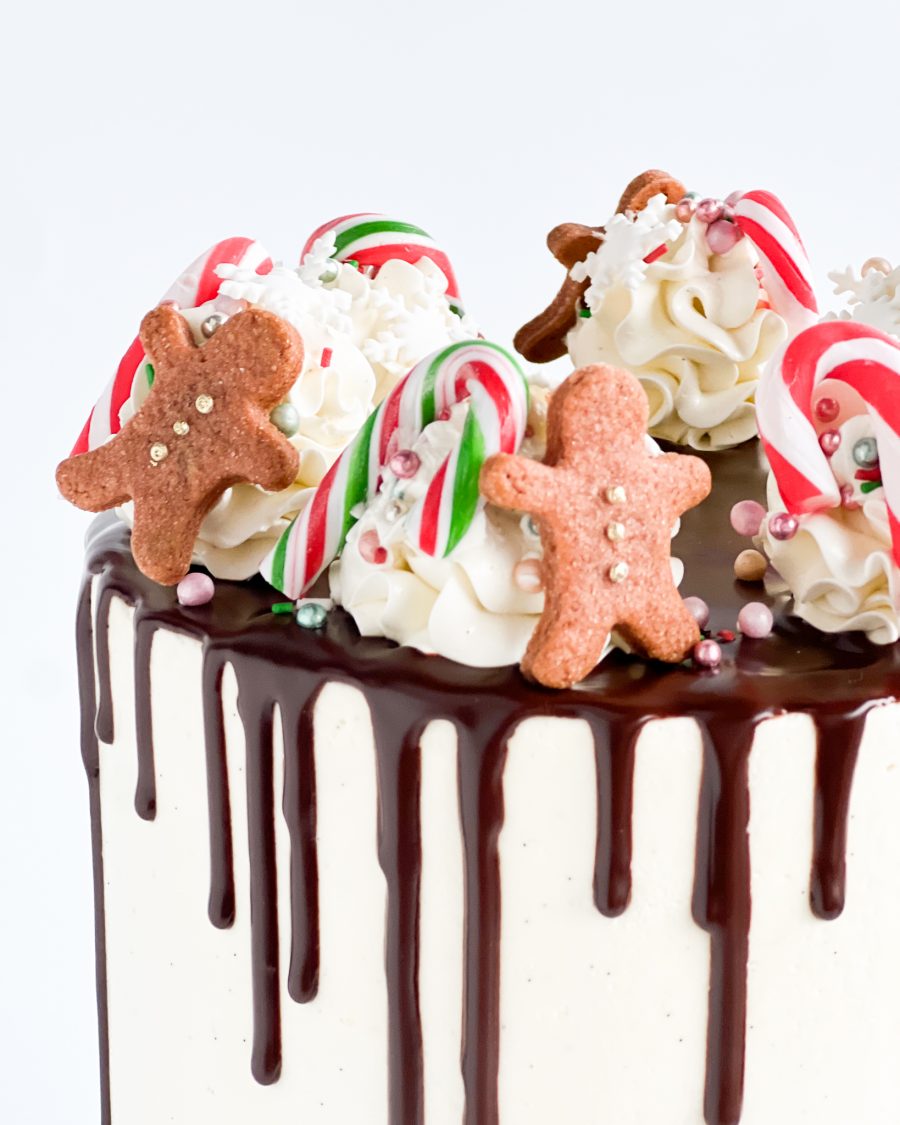 Close-up view of a festive Christmas cake decorated with chocolate ganache drips, tiny gingerbread men, and candy canes, showcasing intricate holiday details.