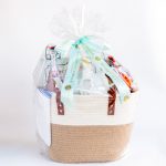 A cream and natural brown woven tote bag filled with Mother's Day treats including a wildflower bouquet, Bobbette & Belle recipe book, sparkling lemonade, decorative pastel vanilla cupcake, fresh blueberry scones, Earl Grey tea and a china teapot