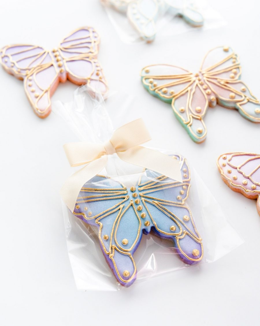 An overhead shot of a selection of gorgeous rainbow pastel butterfly sugar cookies with outline piping in gold.