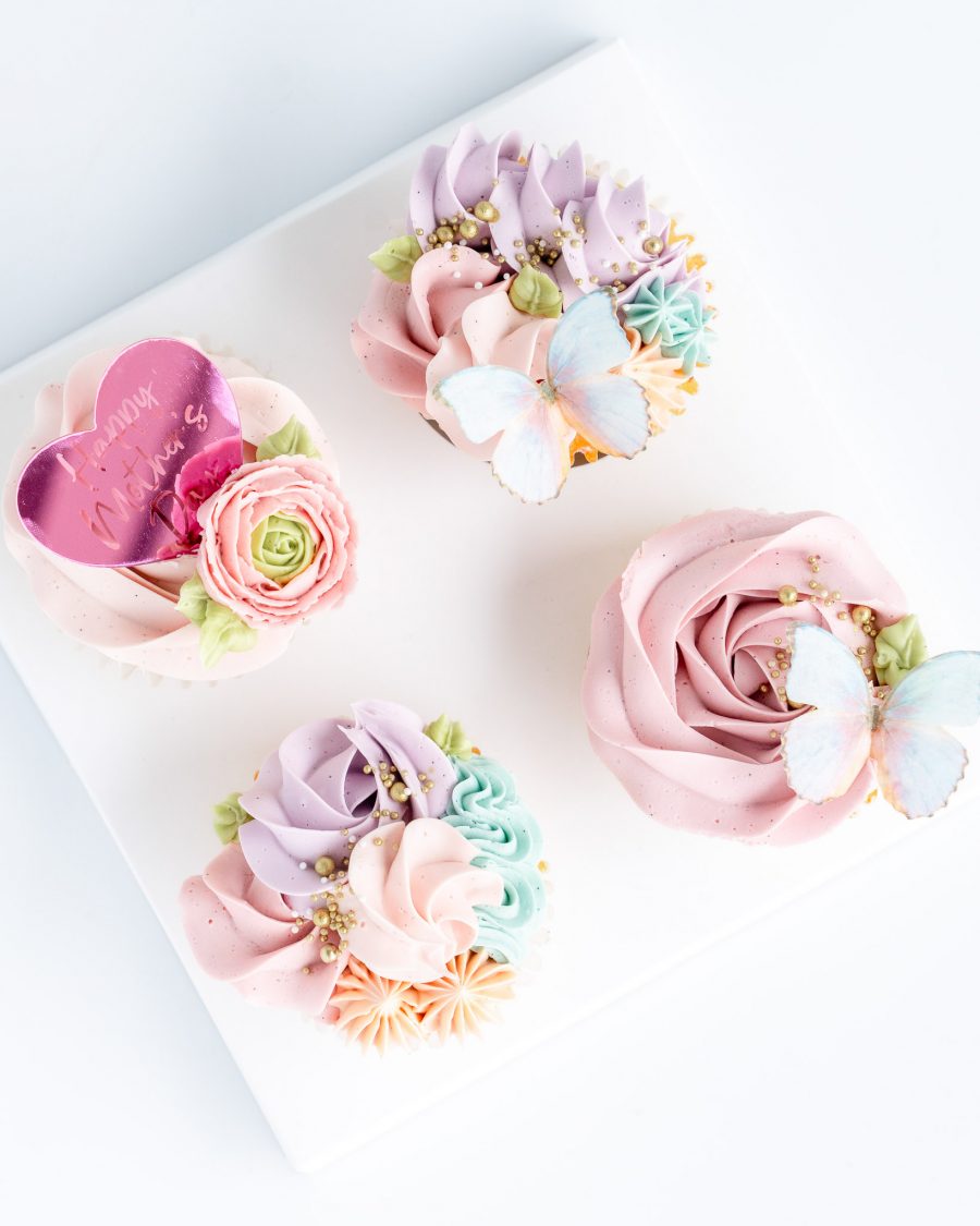 Vanilla Rose swirl cupcakes with Happy Mother's Day heart shaped plaque, sugar butterfly and decorative buttercream piping in shades of soft pink, blue lavender and turquoise