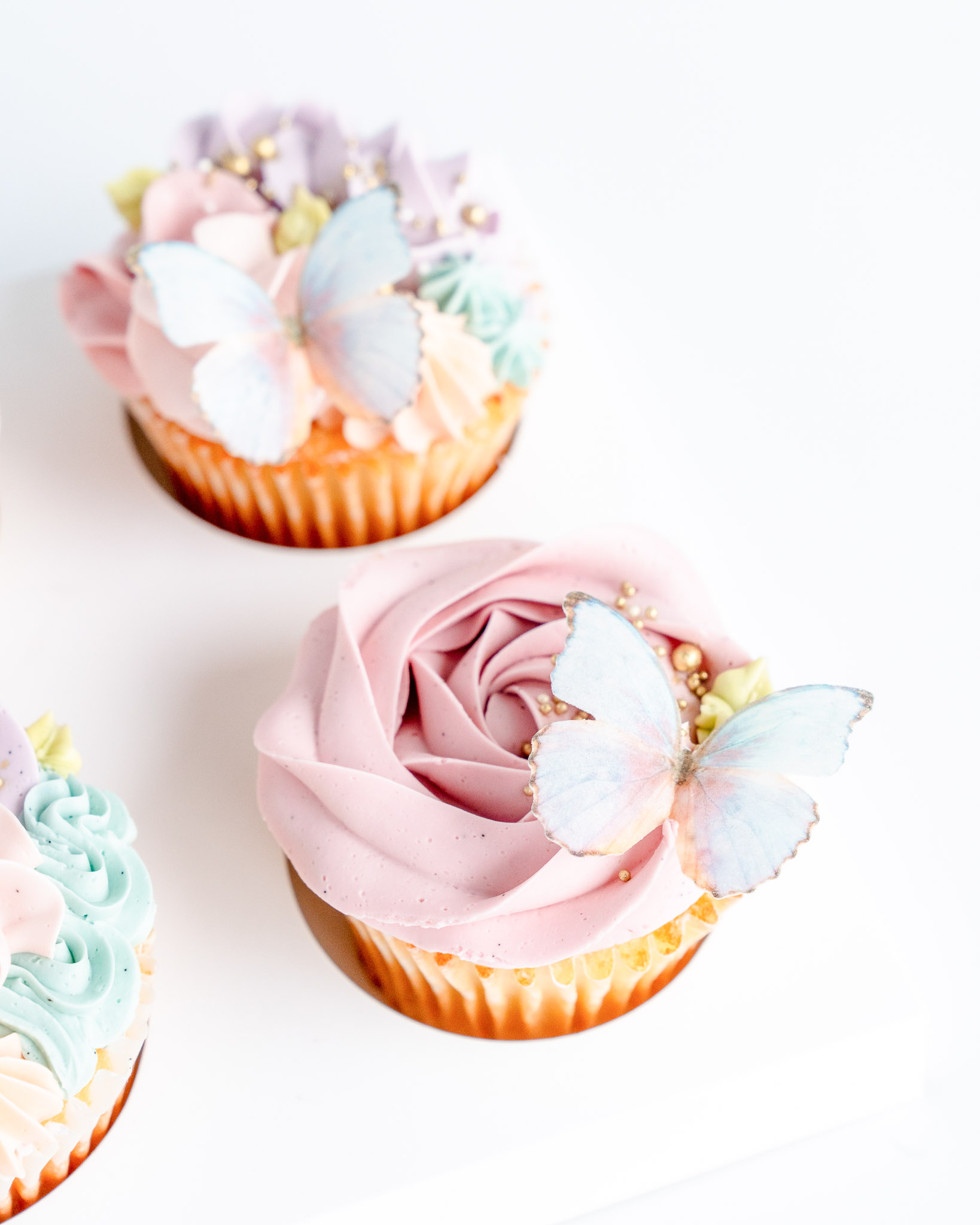 Rose swirl cupcake with sugar butterfly and buttercream piping in shades of soft pink, blue lavender and turquoise