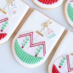 Close-up view of festive ornament sugar cookies featuring delicate Christmas ornament designs in red and green with golden bows and holiday-themed tags