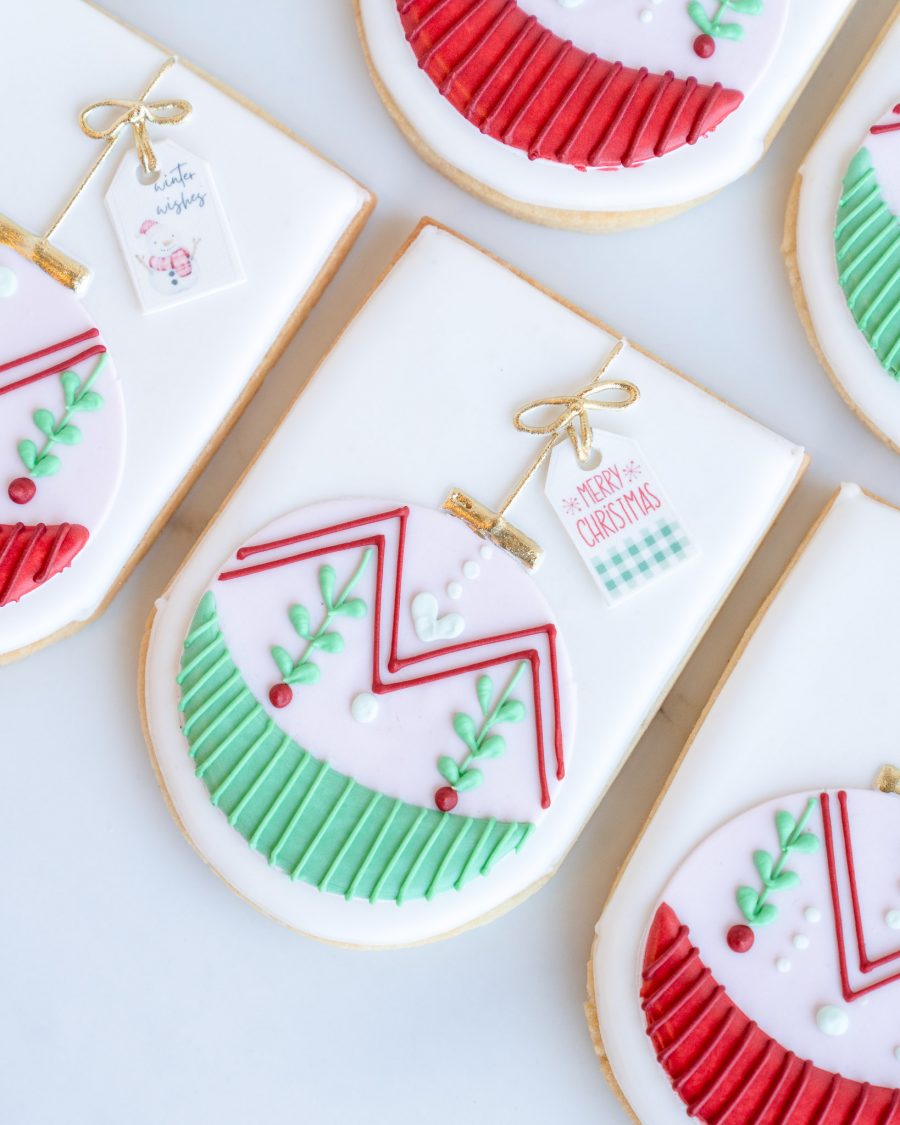 Close-up view of festive ornament sugar cookies featuring delicate Christmas ornament designs in red and green with golden bows and holiday-themed tags