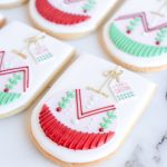 Hand-decorated festive ornament sugar cookies with intricate red and green patterns, golden accents, and mini holiday tags, arranged on a marble surface