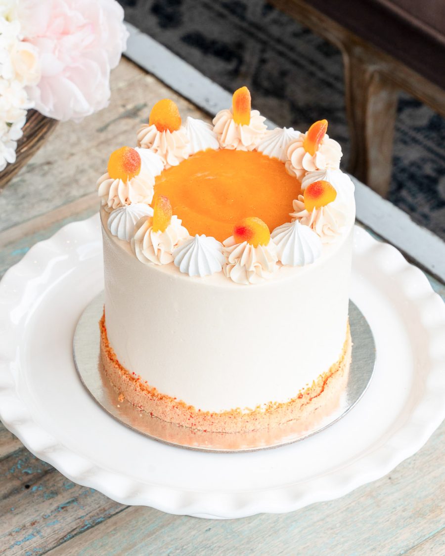 Peaches and Cream Cake topped with peach purée, meringues, buttercream swirls, and fuzzy peach candy on a white plate.