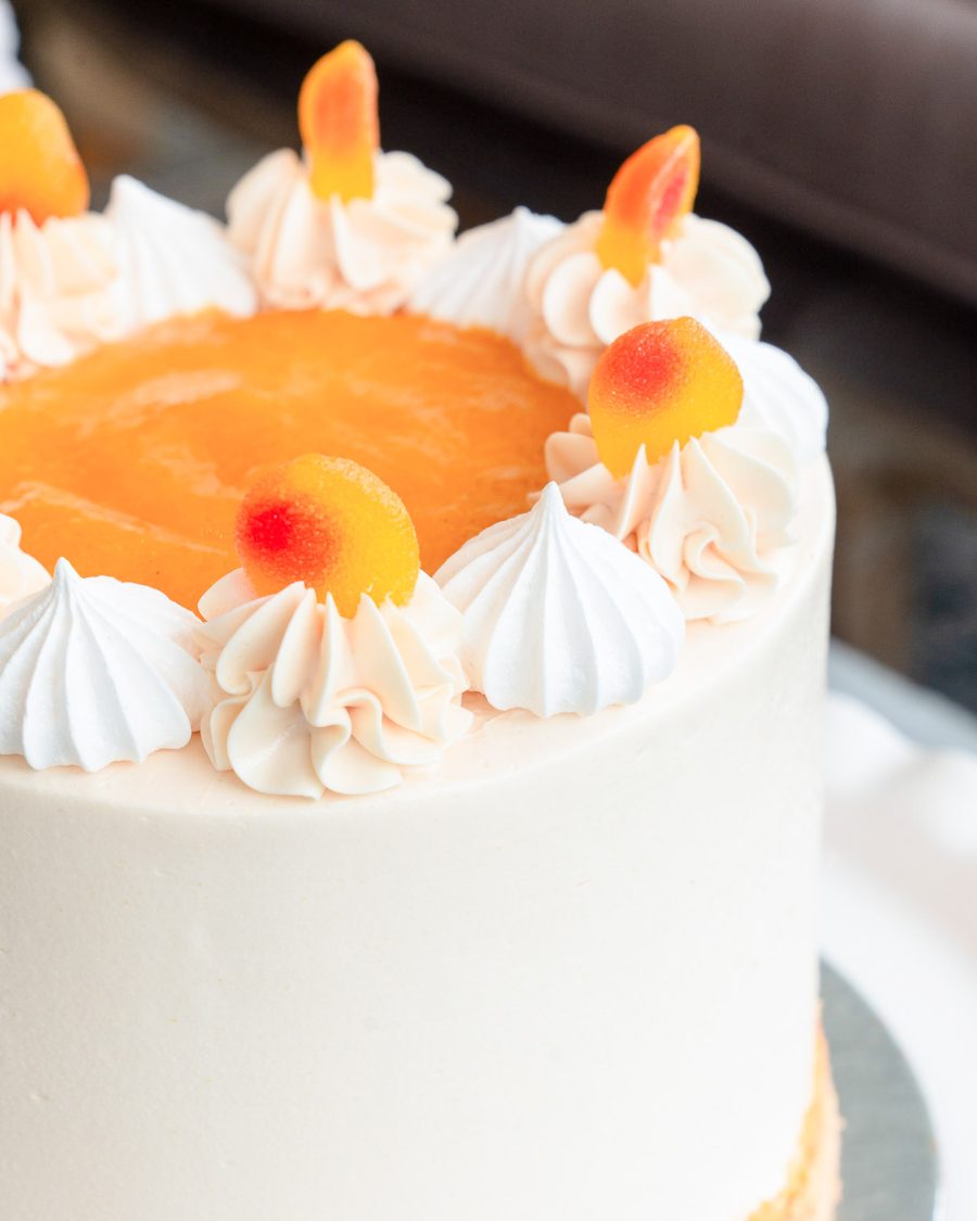 Detailed view of the Peaches and Cream Cake showing peach purée, buttercream swirls, meringues, and fuzzy peach candy.