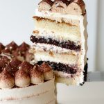 A slice of tiramisu cake showing layers of vanilla and chocolate sponge, mascarpone cream, and espresso-soaked filling.