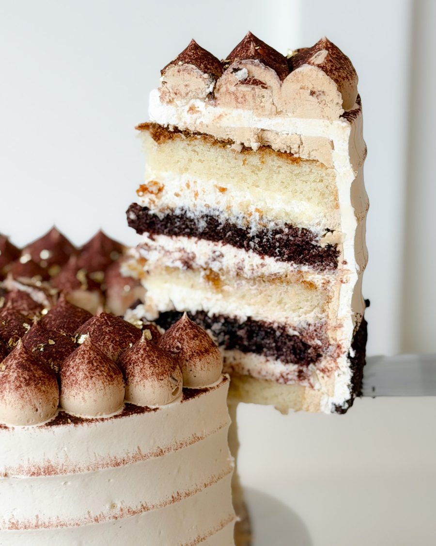 A slice of tiramisu cake showing layers of vanilla and chocolate sponge, mascarpone cream, and espresso-soaked filling.