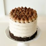 Elegant tiramisu cake with layers of chocolate and vanilla sponge, topped with cocoa-dusted mascarpone cream and gold flakes.