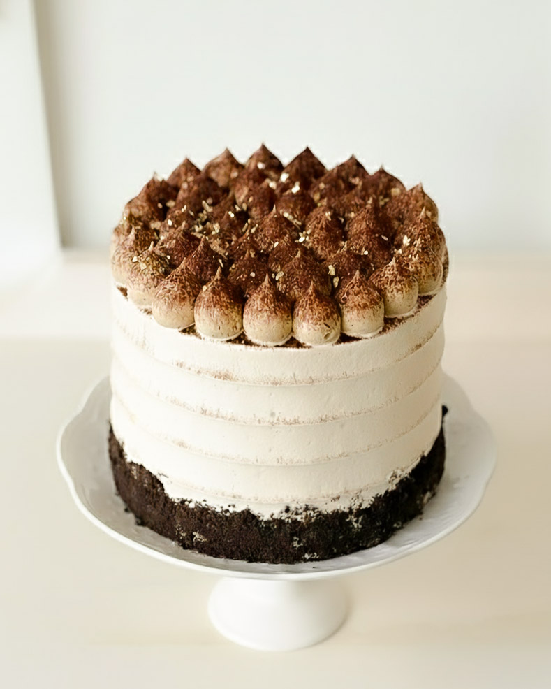 Elegant tiramisu cake with layers of chocolate and vanilla sponge, topped with cocoa-dusted mascarpone cream and gold flakes.