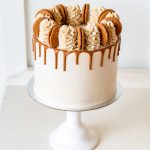 Front view of a Biscoff cake with vanilla frosting, caramel drip, and cookie garnish