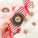 Hand holding a red-and-white striped Bobbette & Belle holiday caramel cracker with gold and black artisanal label.