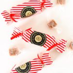 Three festive red-and-white striped Bobbette & Belle holiday caramel crackers surrounded by individually wrapped caramels.