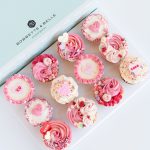 Box of 12 Valentine’s cupcakes decorated with tinted vanilla buttercream swirls and romantic heart toppers.