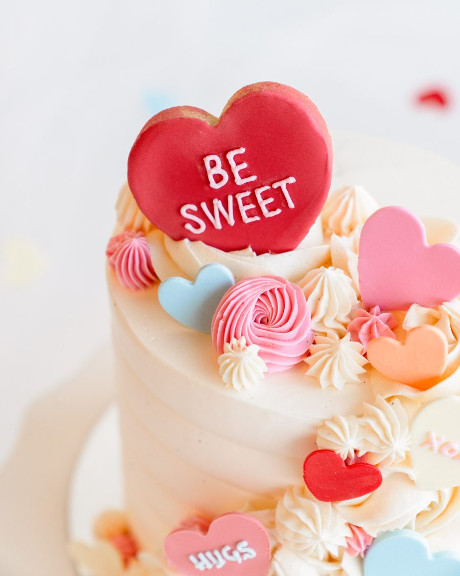 Close-up of pastel candy hearts and piped frosting on a Valentine's mini cake.