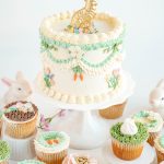Easter bunny cake with floral buttercream piping and golden chocolate bunny topper surrounded by decorated cupcakes