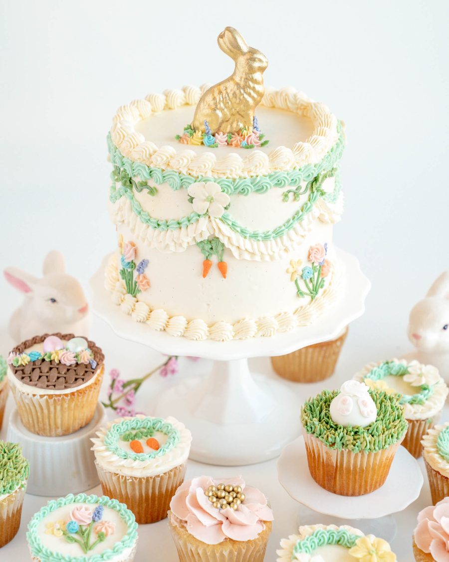 Easter bunny cake with floral buttercream piping and golden chocolate bunny topper surrounded by decorated cupcakes