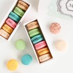 Assorted pastel French macarons in gift boxes with colourful flavours displayed on a clean white background