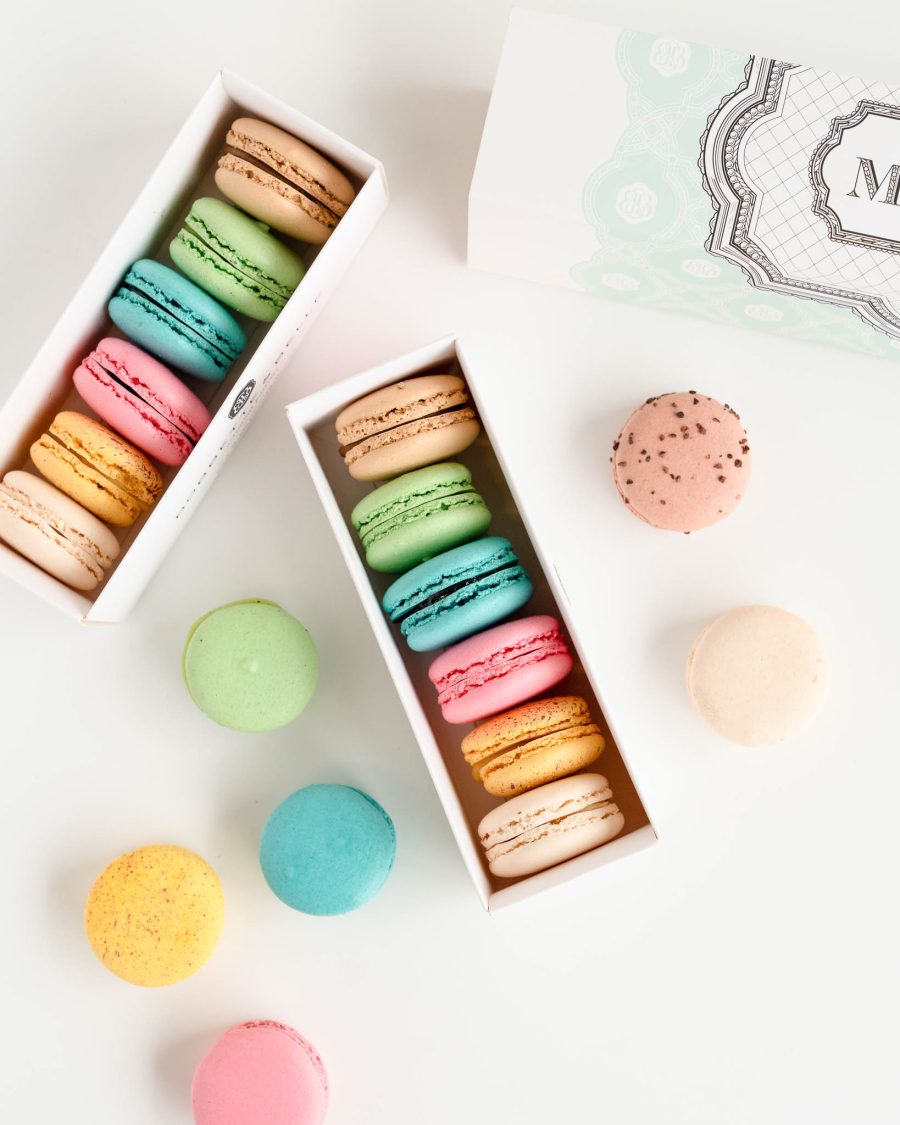 Assorted pastel French macarons in gift boxes with colourful flavours displayed on a clean white background