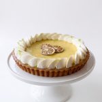 Handmade lime curd tart topped with piped cream, lime zest and dried lime slices on a white cake stand.