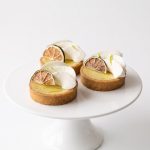 Individual Key lime tarts with piped cream, lime zest and dried lime slices on a white cake stand.